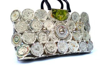May include: A white handbag made from rolled up newspaper with a black handle and gold accents. The bag has a gold metal plate with the word "Anya" on it.