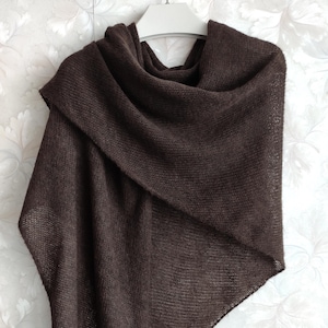 May include: A dark brown knitted shawl with a lightweight, semi-sheer texture. The garment features a triangular shape with a soft, loose weave and is draped over a white hanger, displaying a consistent solid color throughout the entire piece.