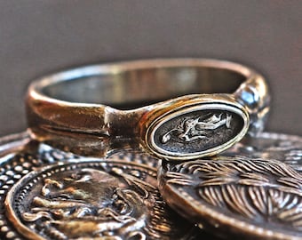 May include: A silver ring with an oval-shaped design featuring a raised image of a person. The ring is sitting on top of several antique coins.