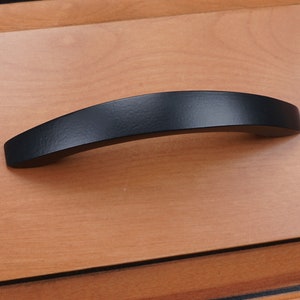 May include: Black arched cabinet pull with a smooth, slightly textured finish.
