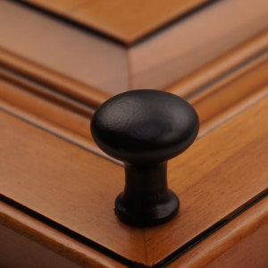 May include: A black wooden knob with a rounded top, mounted on a wooden surface.