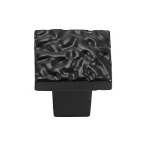 以下が含まれることがあります： テクスチャ加工された表面を持つ黒い正方形のキャビネットノブ。ノブは正方形のベースを持っています。