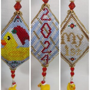 May include: A beaded Christmas bauble with a blue and white diamond-shaped design featuring the year 2021. The bauble has a red and gold trim and a yellow rubber ducky charm hanging from the bottom.