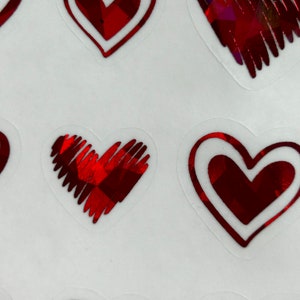 May include: A sheet of red heart stickers with a holographic finish. The hearts have a white outline and are arranged in a random pattern.