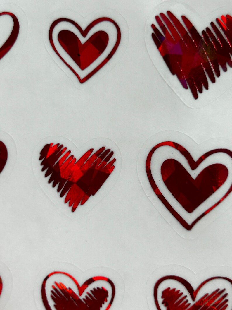May include: A sheet of red heart stickers with a holographic finish. The hearts have a white outline and are arranged in a random pattern.