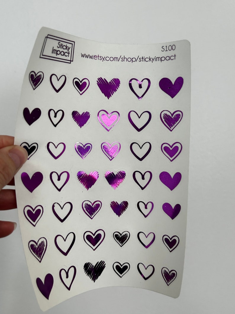 May include: A sheet of purple heart stickers with different designs. The stickers are on a white background. The sheet has the text "Sticky Impact" and "www.etsy.com/shop/stickyimpact" printed on it.