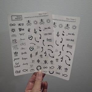 May include: Two white sticker sheets with black illustrations and text. The stickers include arrows, hearts, stars, and phrases like "Yes," "Love This," and "Faith." The sheets are labeled "Bible Margin 1" and "Sticky Impact."