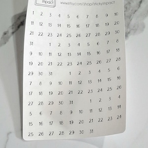 May include: A white sheet of paper with black numbers 1 through 31 printed in rows. The numbers are arranged in a calendar format. The paper has the text "Sticky Impact" and a website address printed at the top.
