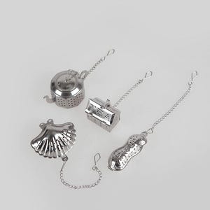 May include: Four stainless steel tea infusers in different shapes: a teapot, a house, a seashell, and a peanut. Each infuser has a chain attached.