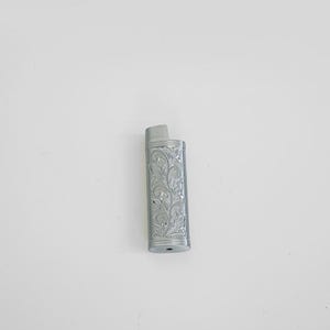 Puede incluir: Un encendedor plateado con un diseño floral grabado.
