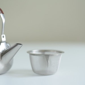 Może przedstawiać: Srebrny czajnik z brązowym sk&oacute;rzanym uchwytem i pasującym srebrnym sitkiem do herbaty.