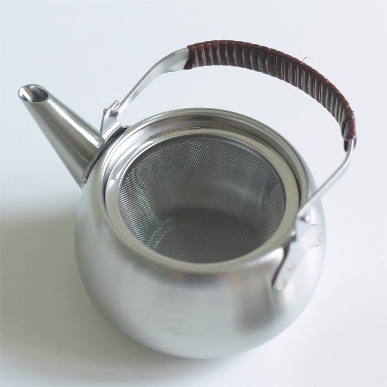 Może przedstawiać: Srebrny czajnik z wbudowanym sitkiem i brązowym sk&oacute;rzanym uchwytem.