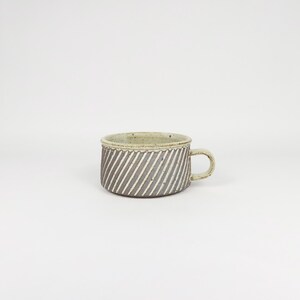 Könnte beinhalten: Eine Keramik-Tasse mit einem grau-weißen diagonal gestreiften Muster. Die Tasse hat einen kleinen Henkel und einen hellgrünen Rand. Die Tasse hat einen Durchmesser von ca. 10 cm und ist 8 cm hoch.