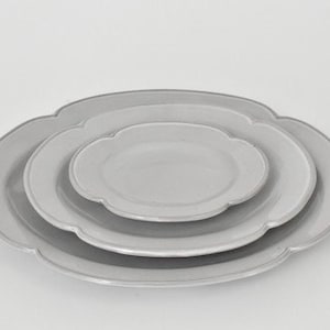May include: A set of three grey ceramic plates with scalloped edges. The plates are nested inside each other, with the smallest plate in the centre.