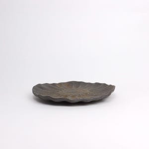 Puede incluir: Peque&ntilde;o plato de cer&aacute;mica gris oscuro con borde festoneado. El plato tiene una superficie texturizada y un centro ligeramente elevado, adecuado para servir porciones peque&ntilde;as o como pieza decorativa. Sobre fondo blanco.