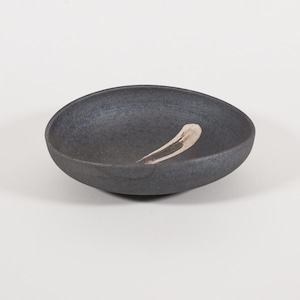 May include: A small, black ceramic bowl with a white glaze design. The bowl is slightly oval shaped and has a rounded bottom.