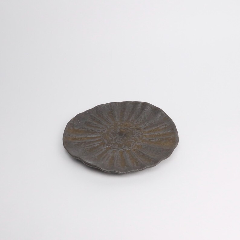 Puede incluir: Un plato de cer&aacute;mica gris oscuro con una superficie texturizada y un dise&ntilde;o de rayos de sol. El plato tiene una forma org&aacute;nica e irregular y probablemente est&aacute; hecho a mano. Es un art&iacute;culo decorativo.