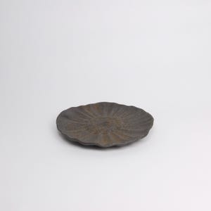 Puede incluir: Un plato de cer&aacute;mica gris oscuro con un patr&oacute;n radial texturizado. El plato tiene una forma org&aacute;nica ligeramente irregular y est&aacute; sobre un fondo blanco. El plato tiene aproximadamente 20 cm de di&aacute;metro.