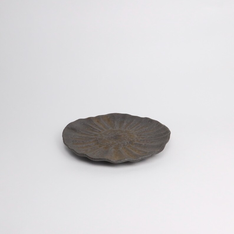 Puede incluir: Un plato de cer&aacute;mica gris oscuro con un patr&oacute;n radial texturizado. El plato tiene una forma org&aacute;nica ligeramente irregular y est&aacute; sobre un fondo blanco. El plato tiene aproximadamente 20 cm de di&aacute;metro.