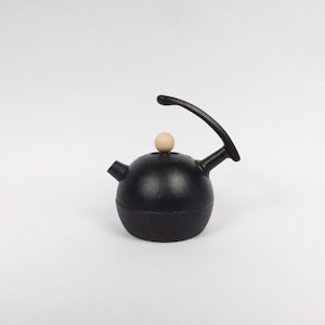 May include: Black cast iron kettle with a wooden knob on the lid and a curved handle.