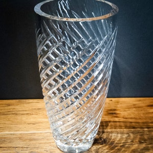 May include: A clear glass vase with a spiral cut design. The vase is tall and slender, with a round base.