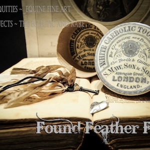May include: A vintage white and blue porcelain container with the text "White Carbolic Tooth Paste" and "S. Maw, Son & Sons, Aldersgate Street, London, England". The container is sitting on an open book with a key and a piece of fabric.