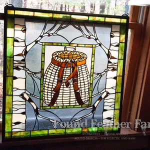 May include: A stained glass window depicting a brown wicker basket with a brown leather strap, surrounded by green and white birch branches. The window is framed in black and has a green and white border. The text "Found Feather Farm" is visible at the bottom of the window.