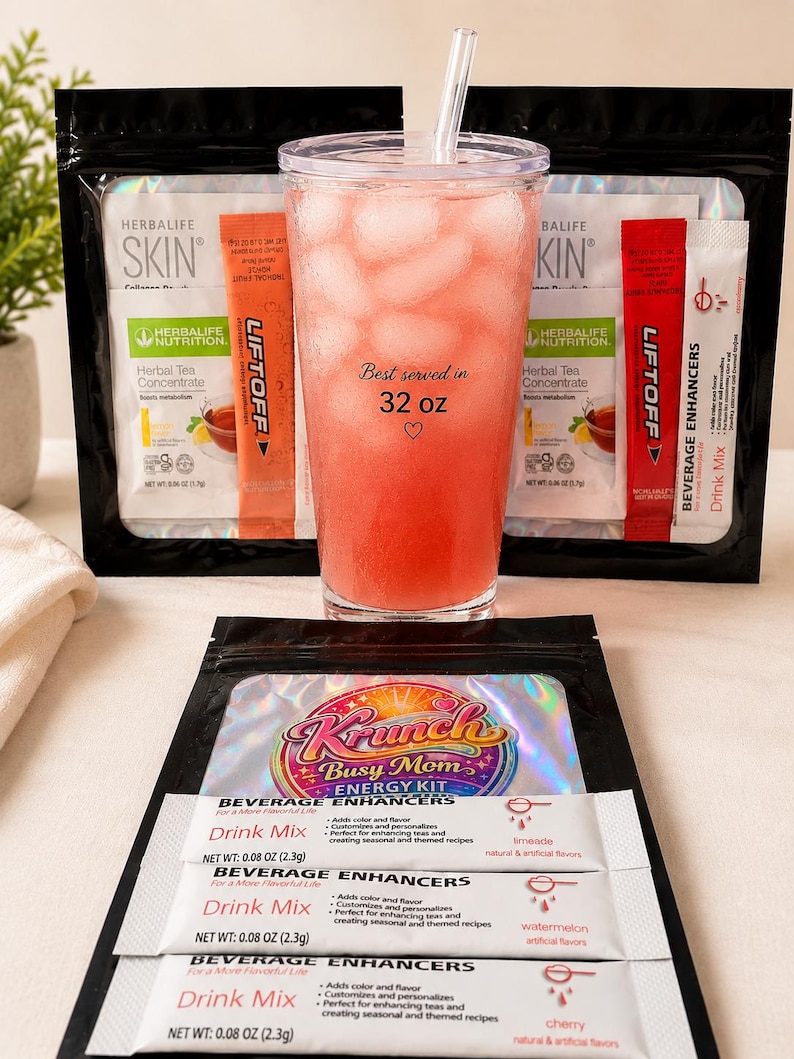May include: A clear plastic tumbler filled with pink liquid and ice, featuring the text 'Best served in 32 oz' with a heart icon. It is surrounded by various Herbalife Skin and Krunch Busy Mom Energy Kit beverage enhancer packets and drink mix sticks.