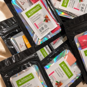May include: Multiple black resealable pouches containing Herbalife Nutrition Herbal Tea Concentrate in raspberry flavor. Each pouch features a clear window displaying the product label with the text Herbal Tea Concentrate, raspberry, and 0.06 oz.