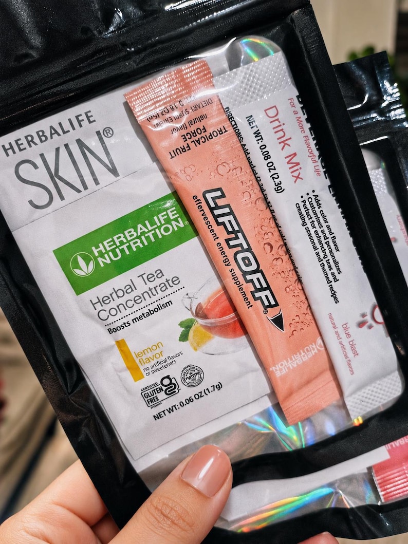 May include: A black pouch containing Herbalife Skin and Nutrition products. Visible items include a Herbal Tea Concentrate packet in lemon flavor, 0.06 oz, and a Liftoff effervescent energy supplement drink mix packet in tropical fruit flavor, 0.08 oz.
