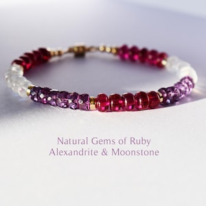 Könnte beinhalten: Ein Armband mit Rubinen, Alexandriten und Mondsteinperlen. Das Armband hat einen goldenen Verschluss und Verbinder. Der Text "Natural Gems of Ruby, Alexandrite & Moonstone" ist unter dem Armband zu sehen.
