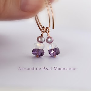 Op de afbeelding: Rosegouden oorringen met alexandriet, parel en maansteen edelstenen. De oorbellen hebben een cluster van paarse, witte en grijze stenen. De tekst "Alexandrite Pearl Moonstone" wordt hieronder weergegeven.