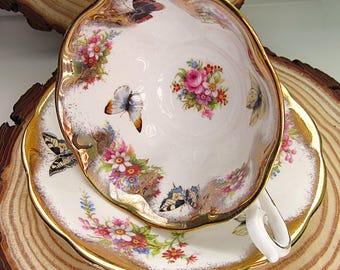May include: A white teacup and saucer set with a gold rim and butterfly and floral designs. The teacup and saucer have a scalloped edge. The teacup has a white handle.