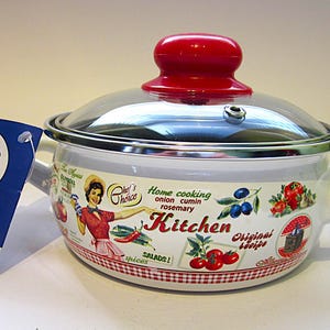 May include: A white enamel kitchen pot with a glass lid and a red knob. The pot has a handle and is decorated with a vintage-style design featuring a woman, vegetables, and the word "Kitchen". A blue tag is attached.