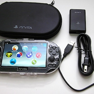 Peut inclure: Une console portable PlayStation Vita noire avec une coque de protection transparente, un étui de transport noir zippé avec le logo PS Vita, un adaptateur secteur Sony noir et un câble de chargement USB noir avec une prise murale standard.