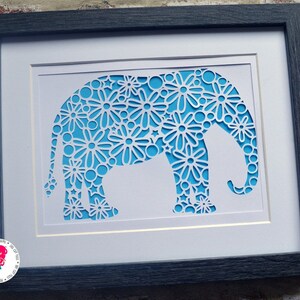 May include: A framed paper cut-out of an elephant, with a blue background and white floral design.