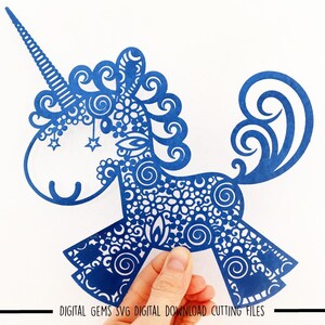 K&ouml;nnte beinhalten: Blauer, filigraner Papierschnitt einer Einhorn mit einem Horn und einem lockigen Schwanz. Das Einhorn ist mit Spiralen und Sternen verziert.