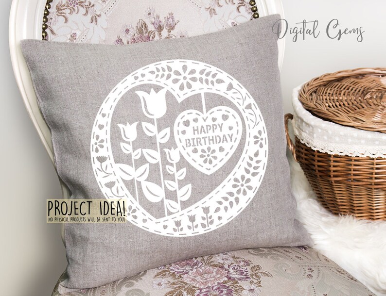 Puede incluir: Una almohada gris con un dise&ntilde;o de corte blanco en forma de coraz&oacute;n con el texto "Happy Birthday" en su interior. El coraz&oacute;n est&aacute; rodeado de flores y hojas. La almohada est&aacute; sobre una silla con un patr&oacute;n floral.