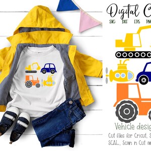 May include: A white t-shirt with a design of various vehicles, including a tractor, a submarine, a car, and a construction vehicle. The design is in blue, orange, and yellow. The t-shirt is on a wooden surface with a yellow raincoat and blue jeans.