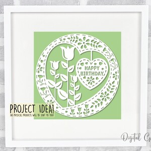 Puede incluir: Un dise&ntilde;o de archivo de corte digital que presenta un c&iacute;rculo con un coraz&oacute;n y flores. El coraz&oacute;n tiene el texto "HAPPY BIRTHDAY" en su interior. El dise&ntilde;o est&aacute; sobre un fondo verde.