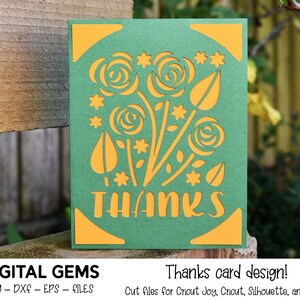 Puede incluir: Una tarjeta verde con un diseño floral amarillo y la palabra "THANKS" recortada. La tarjeta está sobre una superficie de madera.