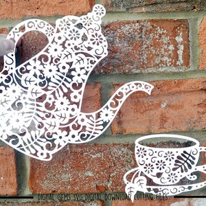 Könnte beinhalten: Weißer Papierschnitt einer Teekanne und einer Teetasse mit filigranen Blumendesigns. Die Teekanne hat einen geschwungenen Ausguss und einen Henkel. Die Teetasse hat einen Henkel und steht auf einem Unterteller.