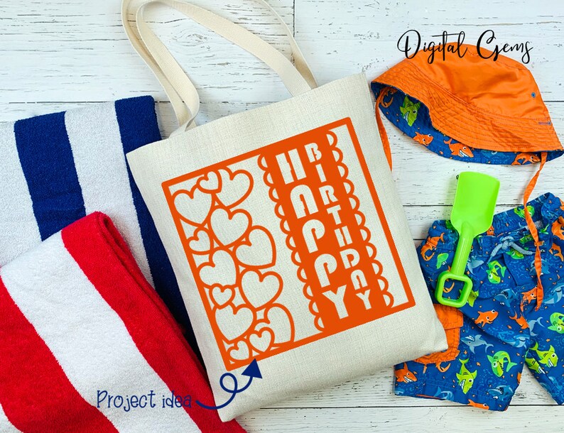 Peut inclure: Un sac fourre-tout en toile blanche avec un motif rouge et blanc qui dit "Joyeux anniversaire" dans un design en forme de c&oelig;ur. Le sac est sur une surface en bois blanc avec une serviette ray&eacute;e bleu et blanc, une serviette ray&eacute;e rouge et blanc, un maillot de bain bleu et orange et un chapeau de soleil orange.