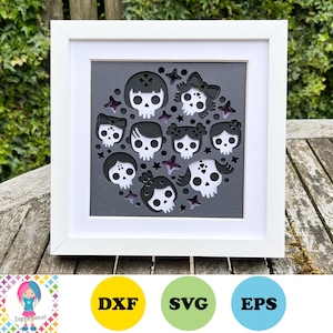 May include: A white frame with a grey background featuring a circle of black and white skull illustrations with bows and flowers. The skulls are arranged in a circle with stars and other decorative elements.