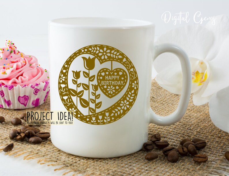Puede incluir: Taza de cer&aacute;mica blanca con un dise&ntilde;o dorado de un coraz&oacute;n con las palabras "Feliz cumplea&ntilde;os" en su interior. El coraz&oacute;n est&aacute; rodeado de flores y hojas.