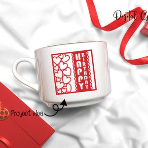 Peut inclure: Une tasse en c&eacute;ramique blanche avec un bord dor&eacute;. La tasse pr&eacute;sente un motif rouge avec les mots "Joyeux anniversaire" et une bordure de c&oelig;urs rouges.