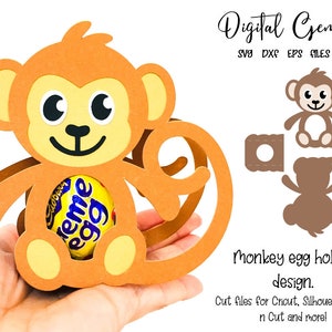 Può includere: Un porta uova a forma di scimmia marrone con un uovo di cioccolato all'interno. Il porta uova è progettato per essere tagliato con una macchina da taglio Cricut, Silhouette, ScanNCut o altra. L'immagine include il testo "Digital Gems SVG DXF EPS FILES" e "Monkey egg holder design. Cut files for Cricut, Silhouette, Scan n Cut and more!"