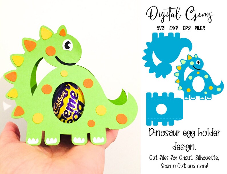 May include: A green dinosaur-shaped egg holder with orange and yellow accents, holding a Cadbury Creme Egg. The design includes the text "Digital Gems" and "Dinosaur egg holder design."