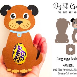 May include: A brown dog-shaped egg holder with black ears, a blue collar, and a Creme Egg inside. The design is made of paper and is held in a hand. Text on the right says "Dog egg holder design."
