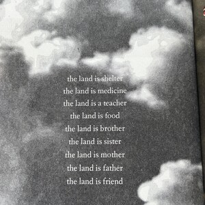 K&ouml;nnte beinhalten: Graustufenbild mit Wolkenhimmel und Text. Der Text lautet: &bdquo;das Land ist Schutz, das Land ist Medizin, das Land ist ein Lehrer, das Land ist Nahrung, das Land ist Bruder, das Land ist Schwester, das Land ist Mutter, das Land ist Vater, das Land ist Freund&ldquo;.